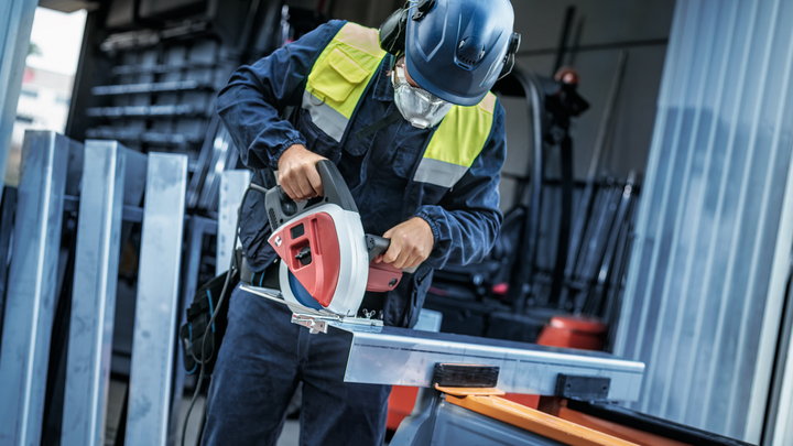 Uma pessoa que usa equipamento de segurança corta uma barra de metal com uma serra circular.