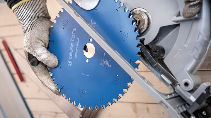 Pessoa que utiliza equipamento de segurança instala uma lâmina de serra circular numa serra de esquadria.