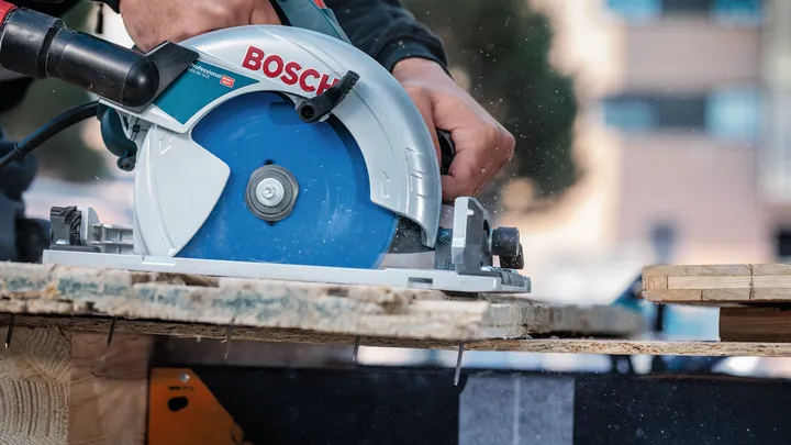 Pessoa que usa equipamento de segurança corta tábuas de madeira com uma serra circular.