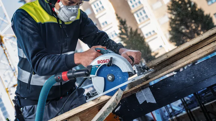 Uma pessoa que utiliza equipamento de segurança corta madeira com uma serra circular num estaleiro de construção.