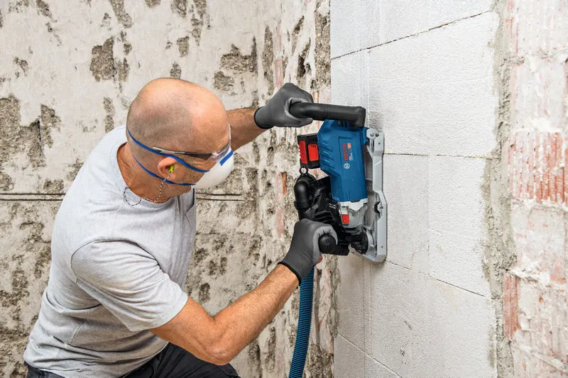 Uma pessoa que utilize equipamento de segurança utiliza uma fresadora de parede numa parede de betão.