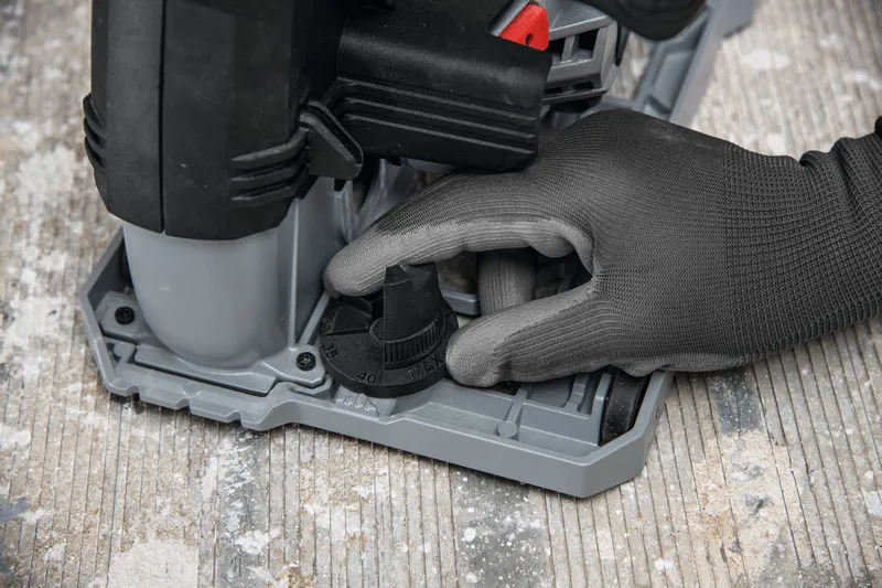 Uma pessoa que utiliza equipamento de segurança ajusta o mostrador de profundidade de uma fresadora de paredes num piso de betão.
