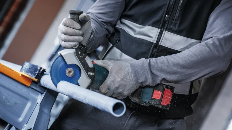 Pessoa que usa equipamento de segurança corta um cano de plástico com uma serra circular.
