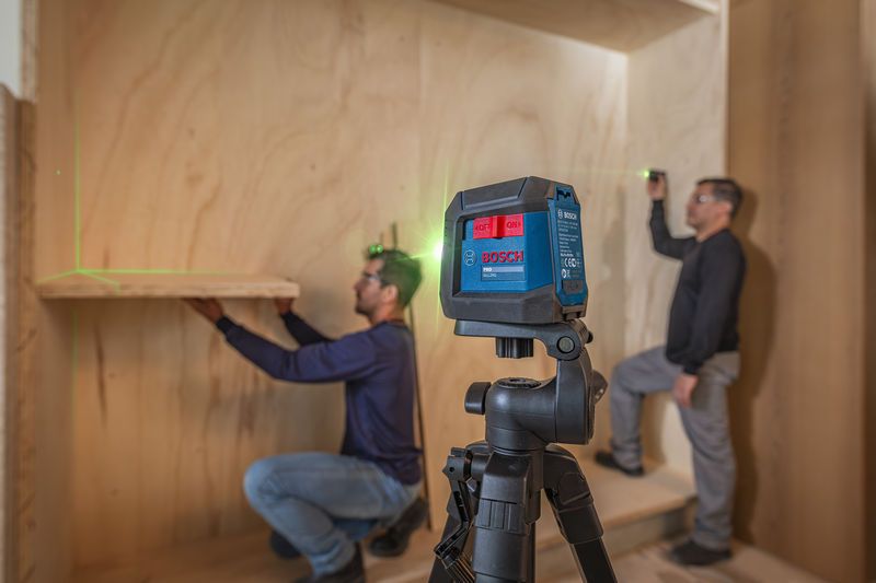 Duas pessoas que utilizam equipamento de segurança utilizam uma ferramenta de nivelamento a laser para instalar prateleiras.