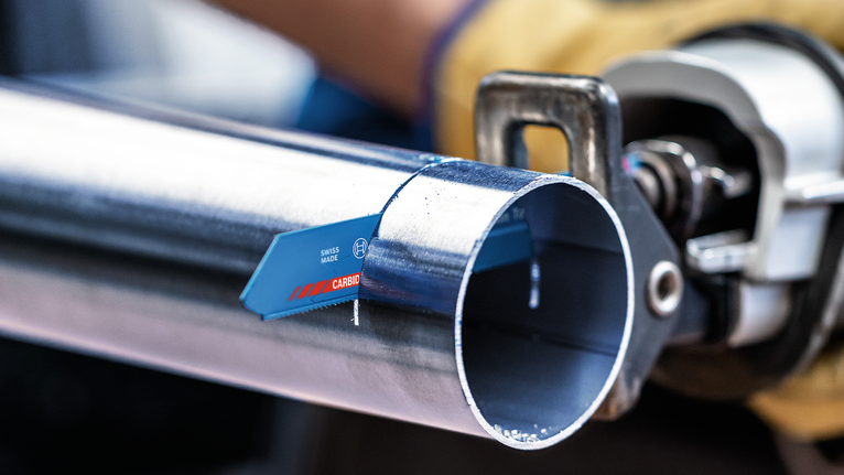 Uma pessoa que utilize equipamento de segurança corta um tubo de metal com uma serra recíproca.