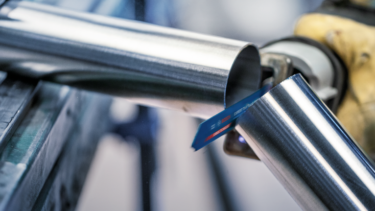 Uma pessoa que utilize equipamento de segurança corta um tubo de metal com uma serra recíproca.