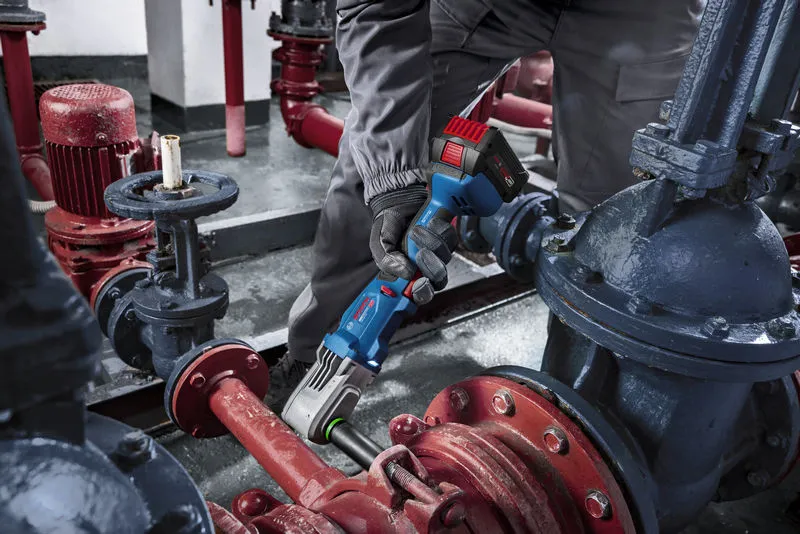 Uma pessoa que utilize equipamento de segurança utiliza uma chave de impacto sem fios em tubagens industriais.