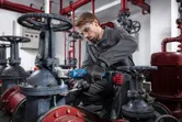 Uma pessoa que utilize equipamento de segurança utiliza uma chave de impacto sem fios para apertar uma válvula num ambiente industrial.