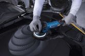 Uma pessoa que usa equipamento de segurança lustra o capô de um carro com uma polidora azul.