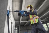 Um operário que utiliza equipamento de segurança perfura uma parede de betão com um martelo rotativo.