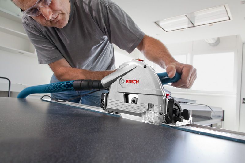 Uma pessoa que utilize equipamento de segurança corta um painel com uma serra de imersão presa a um carril-guia.