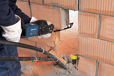 Person wearing safety equipment cuts a brick wall with a reciprocating saw.