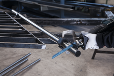 A person wearing safety equipment uses a reciprocating saw to cut a metal pipe.