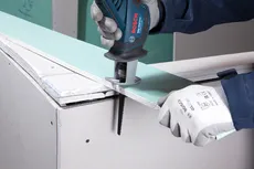 A person wearing safety equipment cuts drywall with a reciprocating saw blade S 641 HM.