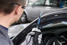 Person wearing safety equipment uses a reciprocating saw to cut a car windshield frame.