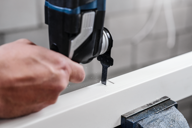 Person uses a jigsaw to cut a rectangular slot in a white board.