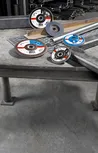 Metal cutting and grinding discs placed on a workbench beside steel pipes and metal sheets.