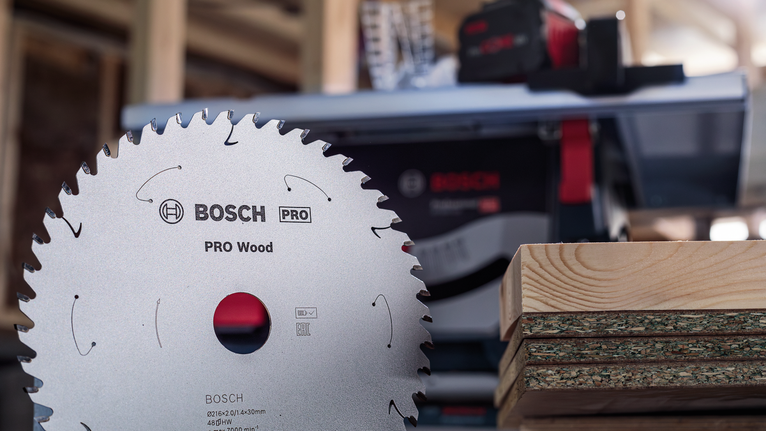 Circular saw blade in front of stacked wood planks in a workshop.