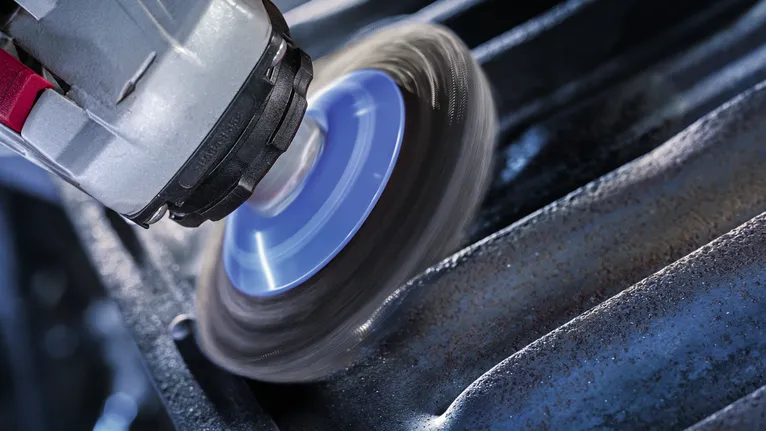 Rotary tool with a wire brush attachment cleans rust from a grooved metal surface.