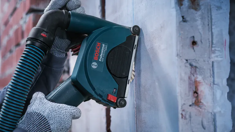 Person wearing safety equipment operates a power wall chaser on concrete.