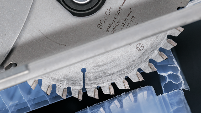 Circular saw blade cutting through blue plastic material.