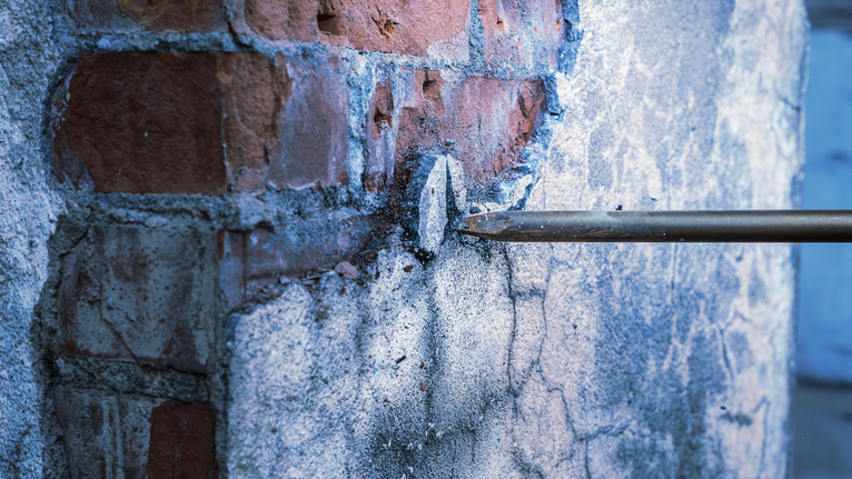 Drill chisel breaking plaster on a brick wall.