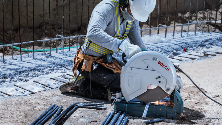Person wearing safety equipment cuts steel rods with a circular saw, producing sparks.
