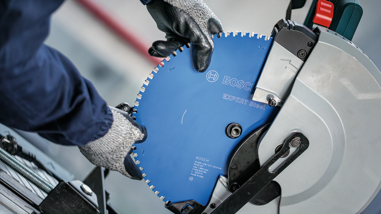 Person wearing safety equipment installs a circular saw blade onto a cut-off machine.
