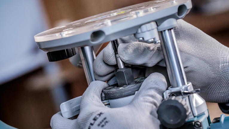 Person wearing safety equipment adjusts a router tool using gloved hands.
