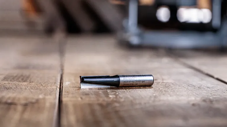 Router bit lying on a wooden surface in a workshop setting.