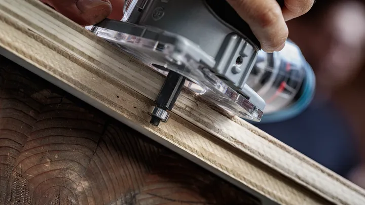 Person trims a wooden board edge with a handheld router tool.