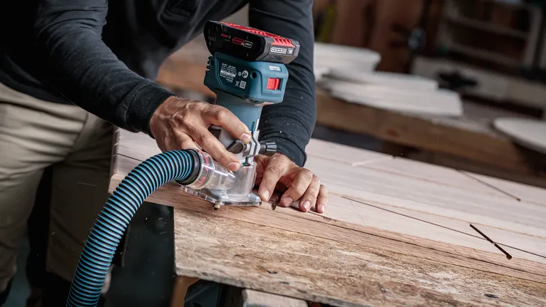 Person guides a cordless wood router along a plank in a workshop.