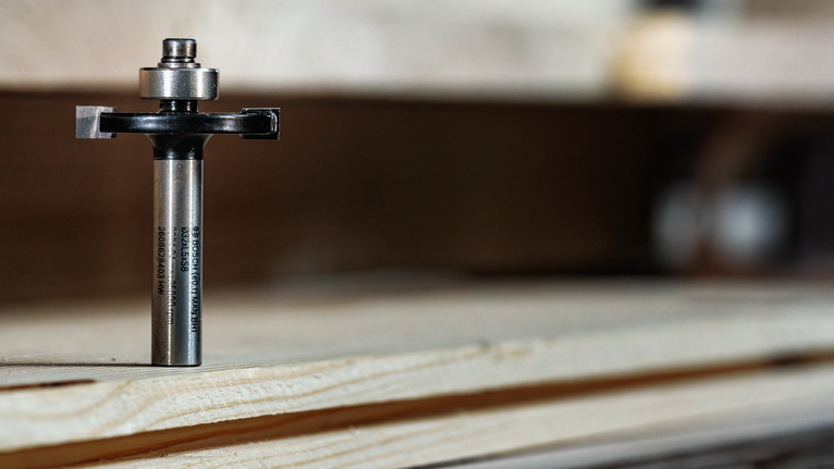 Router bit standing upright on layered wood in a workshop setting.
