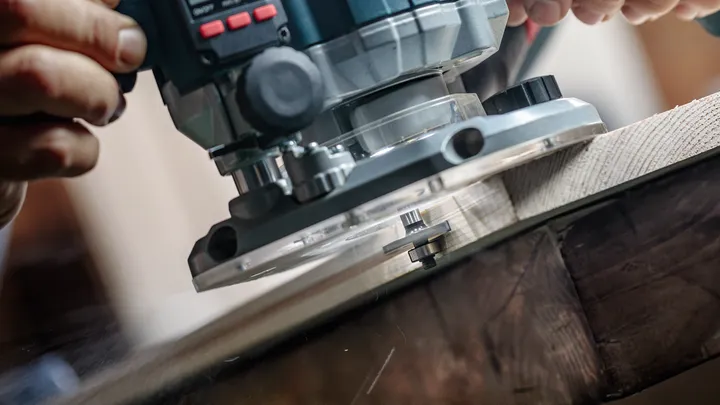 Person guides a power router along wood to create a smooth edge.