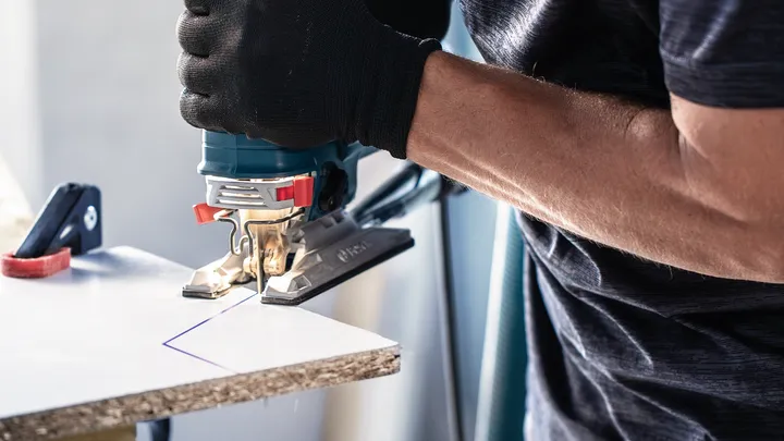 Person wearing safety equipment cuts a marked board with a jigsaw.