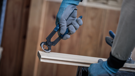 Person wearing safety equipment removes a nail from wood using pliers.