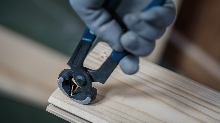Person wearing safety equipment uses pliers to remove a nail from wooden planks.