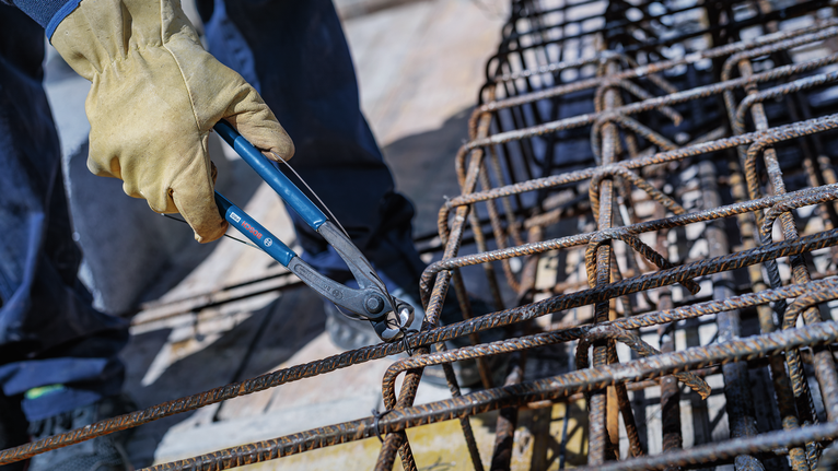 Person wearing safety equipment twists wire around steel rebar with pliers.
