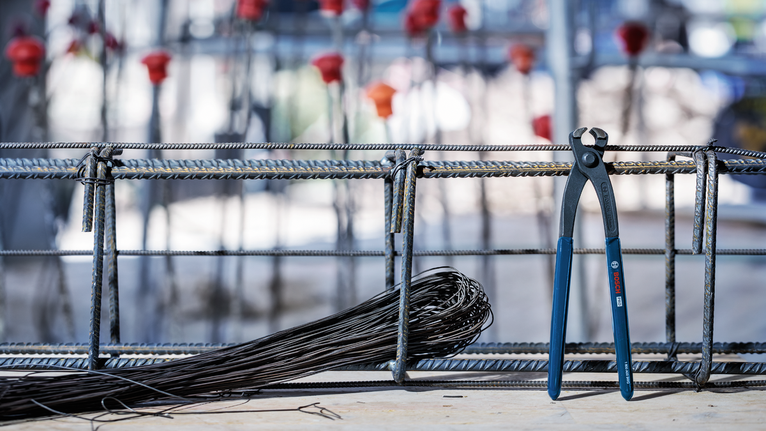 Steel pliers and wire next to a rebar frame at a construction site.