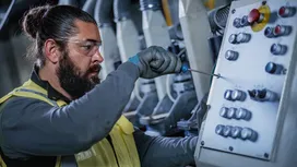 Person wearing safety equipment uses a screwdriver to adjust an industrial control panel.