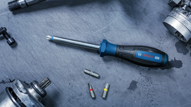 Screwdriver with three bits on a metal surface near mechanical tool parts.
