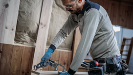 Person wearing safety equipment secures wood to a workbench with a clamp.