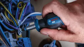 Person tightens a screw among electrical wires using a screwdriver.