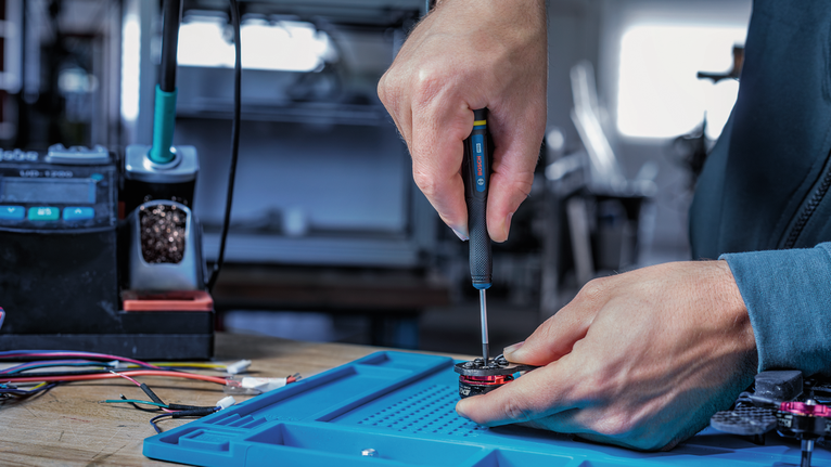 Person assembling an electronic component at a workstation with a screwdriver.