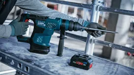 Person wearing safety equipment using a rotary hammer drill on a construction site.