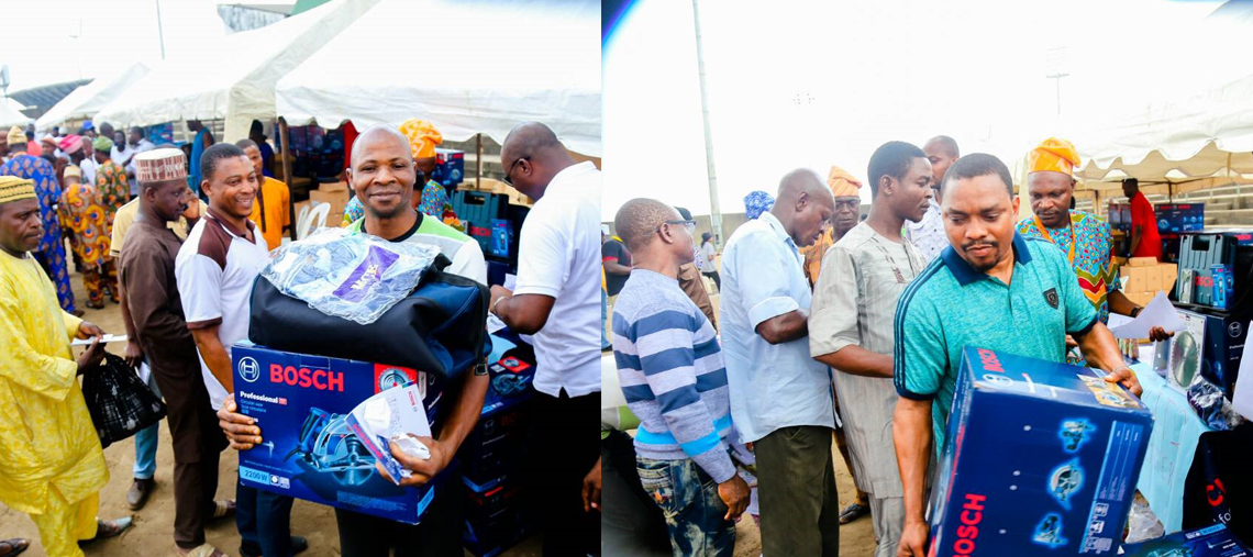 Men hold Bosch tools in a busy outdoor market with colorful tents and excited crowds.