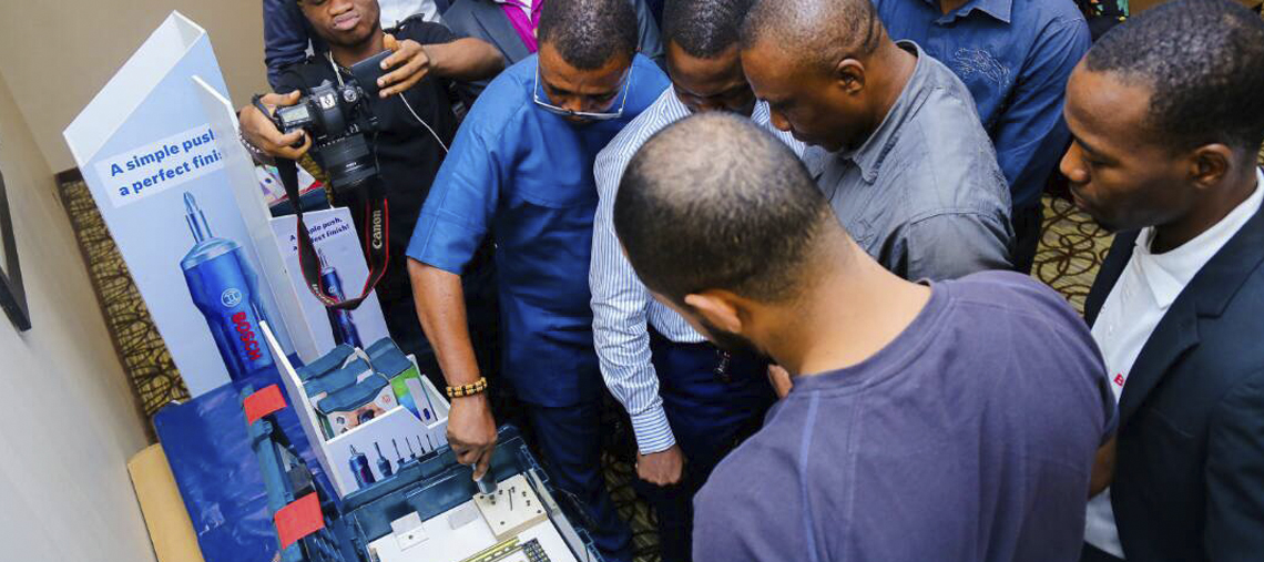 Group of men examining Bosch tools displayed at an event, focused and engaged.