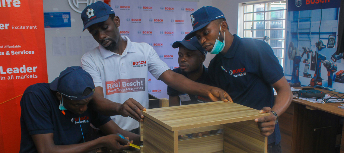 Four men in Bosch uniforms assemble a wooden drawer in a workshop.