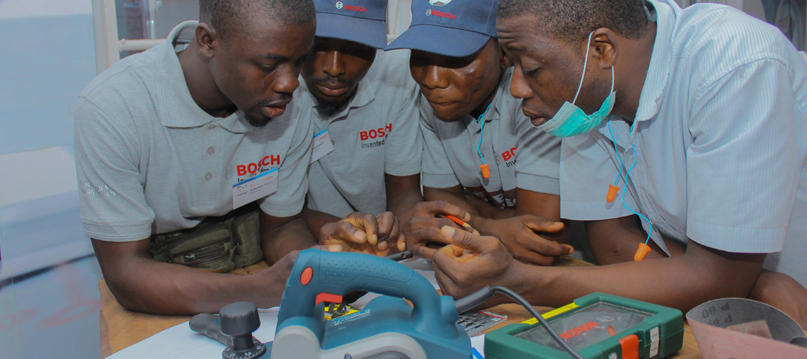 Four men in Bosch shirts examine tools on a table, focused and engaged in discussion.