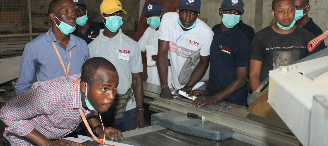 Several men in masks observe Bosch tools in a workshop, focused on training activities.
